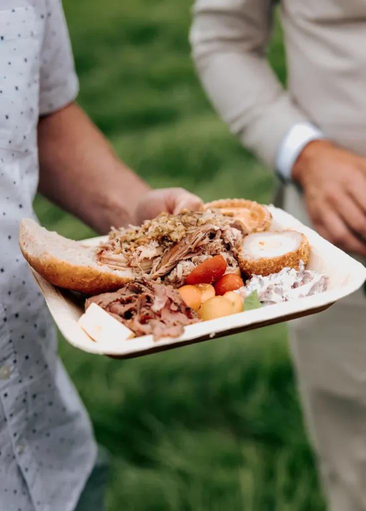 Guest holding a hog roast buffet plate with pulled pork, ham, sausage roll, pork pie and coleslaw